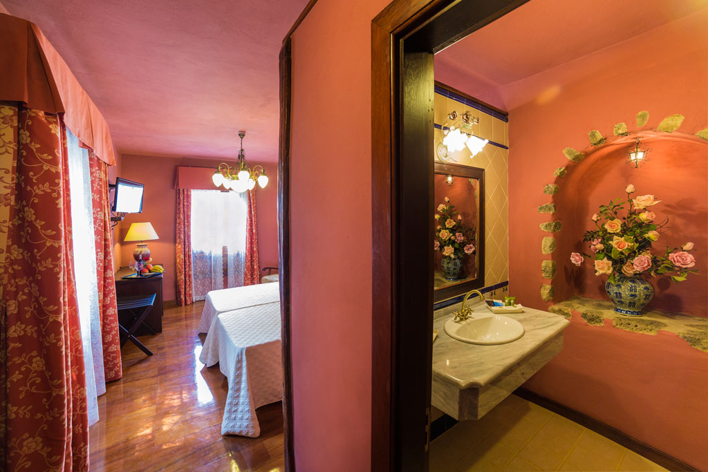 Hotel room in Tenerife with pink decor, floral curtains, and adjacent bathroom.