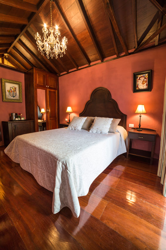 Elegant bedroom with chandelier, wooden accents, and two bedside lamps in Tenerife.