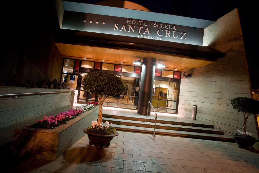 Entrance of Hotel Escuela Santa Cruz in Tenerife at night with plants outside.