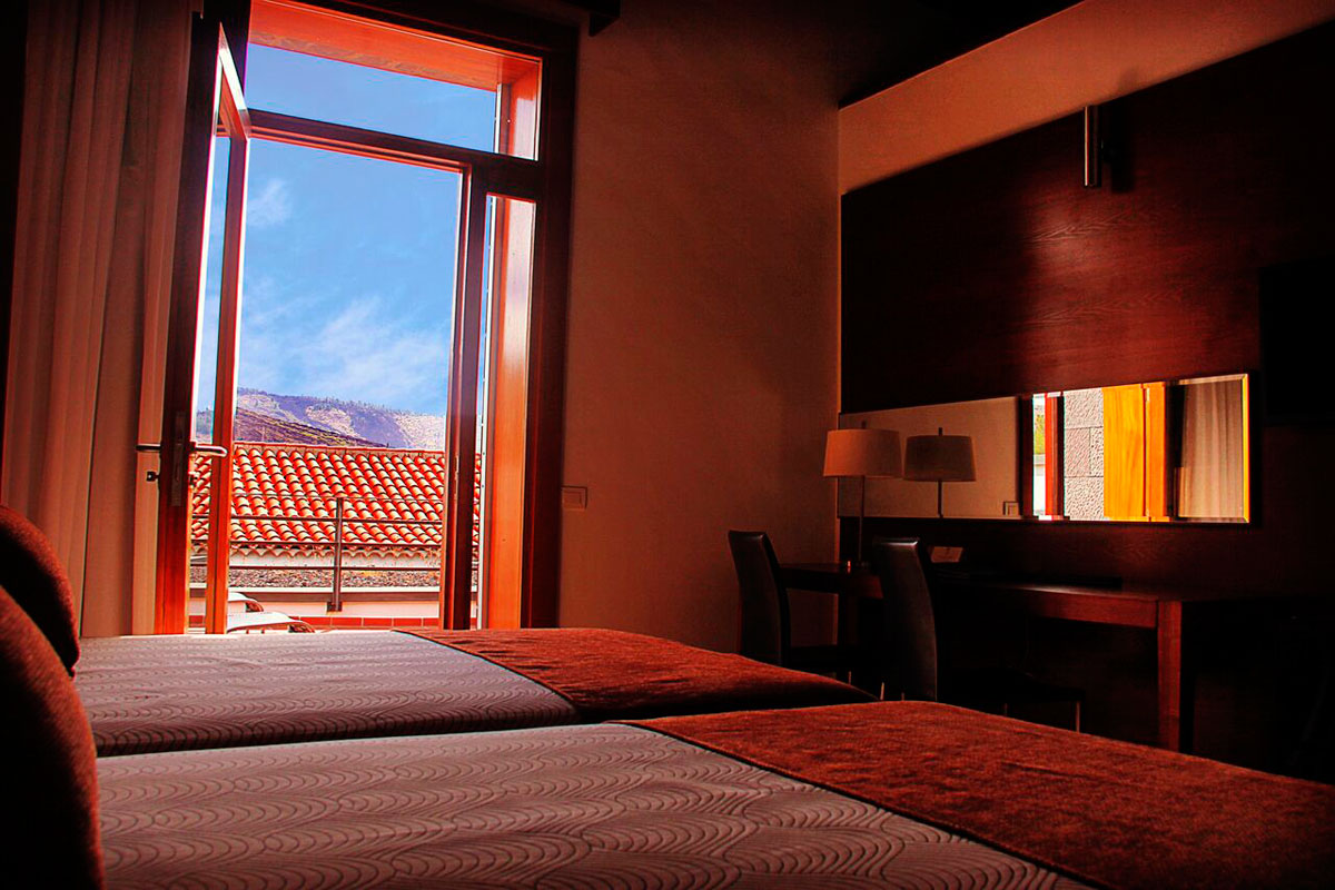 Room with open window view of tiled roof and hills in Tenerife.