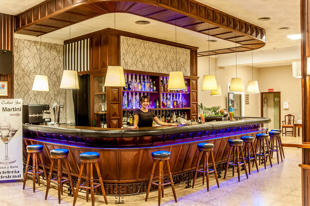 Bartender at a wooden bar in a Tenerife establishment with stools and liquor bottles.