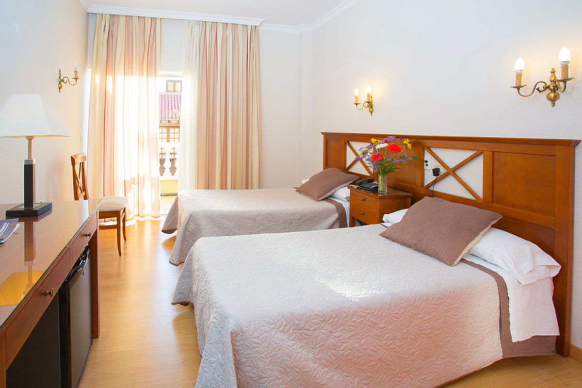 Two twin beds in a hotel room in Tenerife with a small desk and chair.