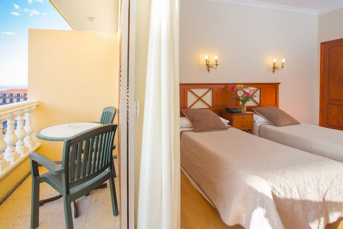 Hotel room with twin beds, balcony view, and chairs in Puerto de la Cruz, Tenerife.