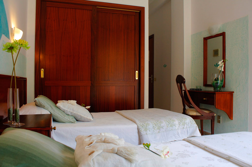 Two neatly made beds in a Tenerife hotel room with wooden closet and vanity.