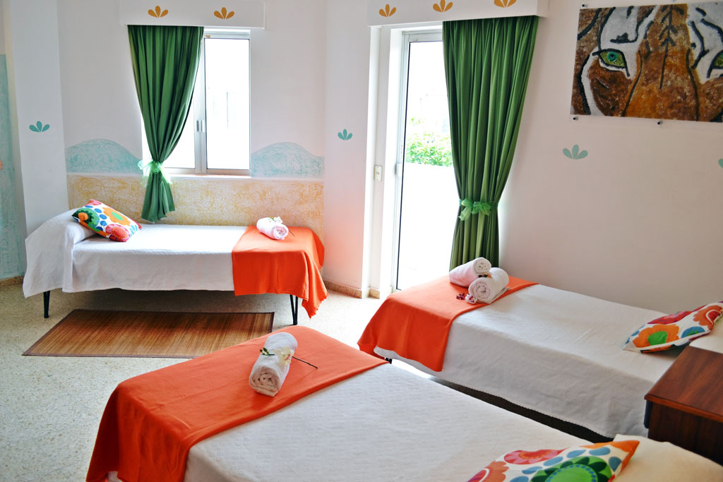 Three beds with orange blankets, colorful cushions, and rolled towels in a room in Tenerife.