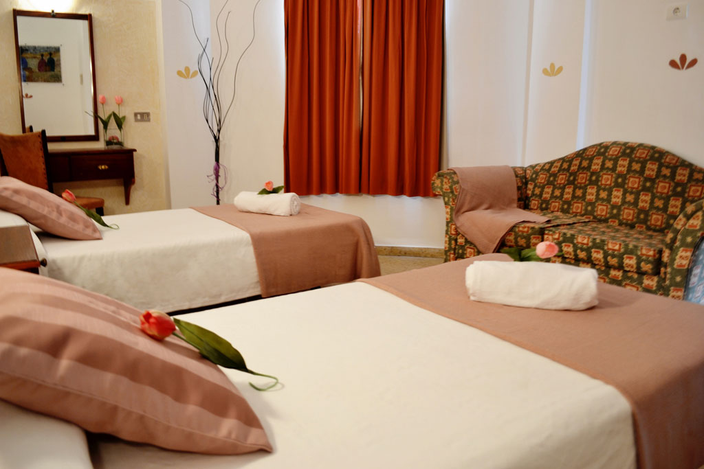 Twin beds with brown covers, decorated with flowers, and a sofa in a Tenerife hotel room.