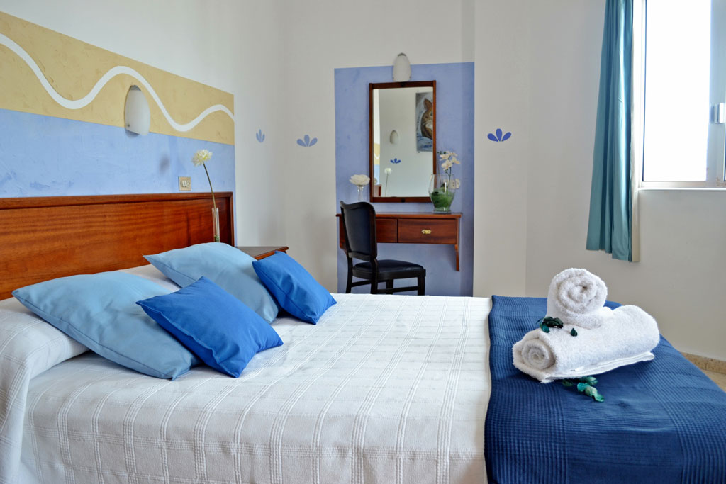 Bedroom with blue pillows and towels, wooden headboard, window view in Tenerife.