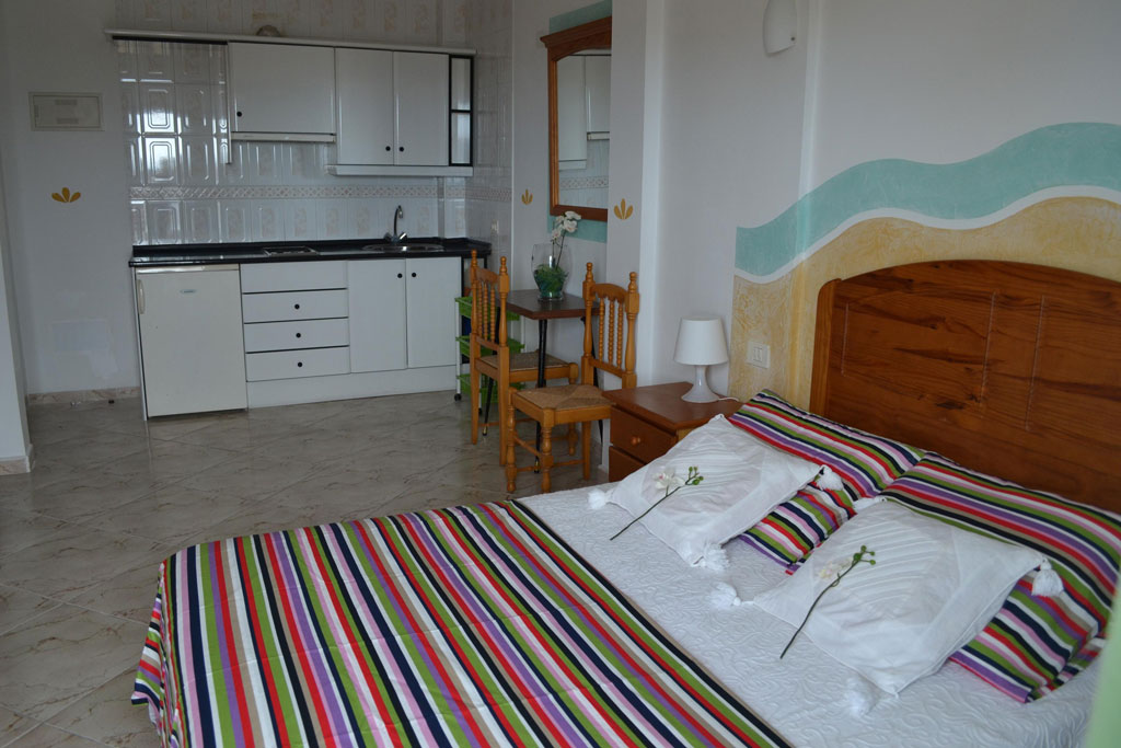Studio apartment with striped bedding, kitchenette, and dining area in Tenerife.
