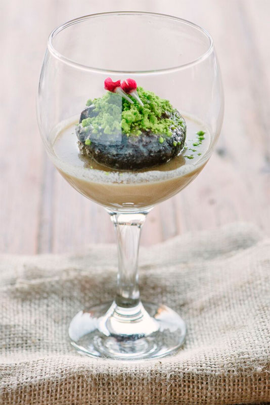 Gourmet dessert in a wine glass with green topping, presented on burlap in Tenerife.