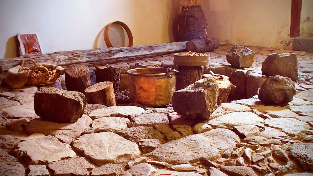 Traditional kitchen setup in Tenerife with stone floor, logs, and a metal pot.