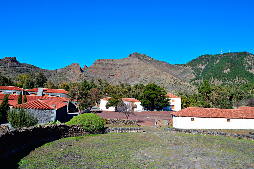 Houses with red roofs surrounded by mountains in Tenerife, clear blue sky above.