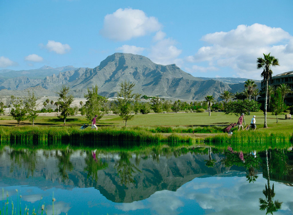 Golfers walking near a pond with mountains in the backdrop in Tenerife.