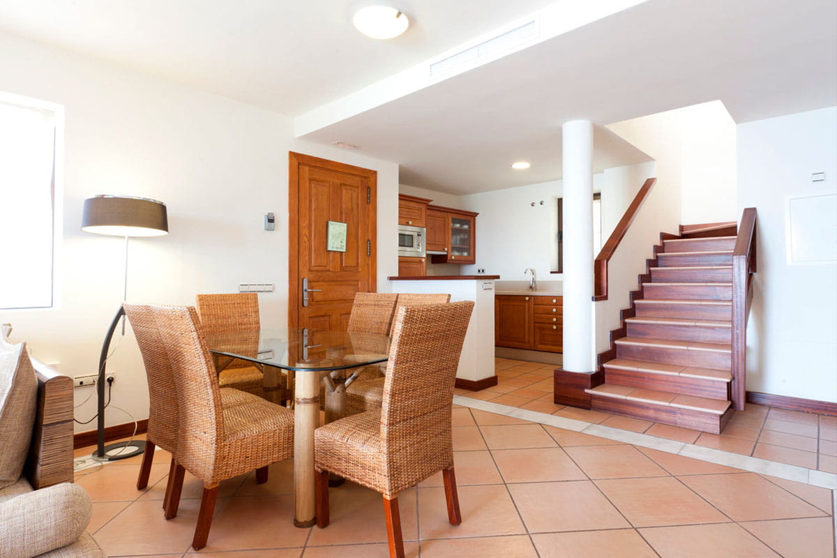 Dining area with glass table and wicker chairs, wooden stairs in Tenerife.