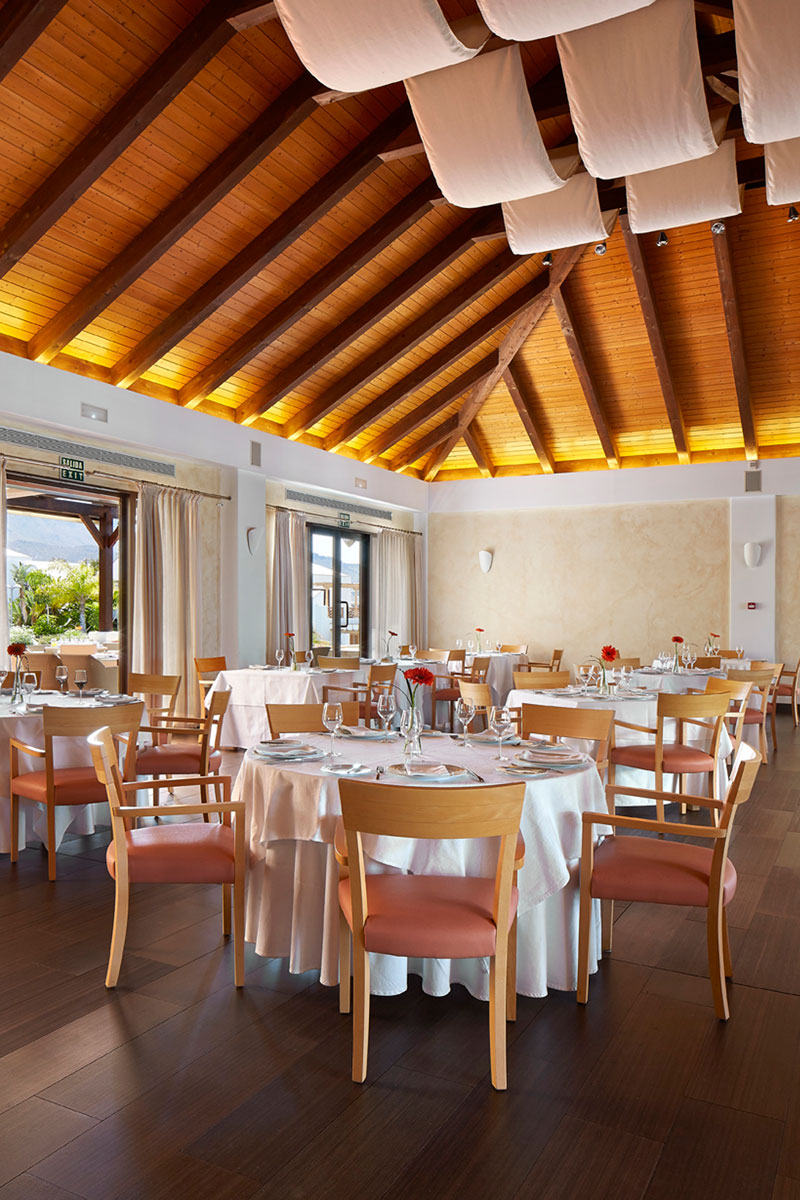 Restaurant dining area in Tenerife with round tables, chairs, and wooden ceiling.