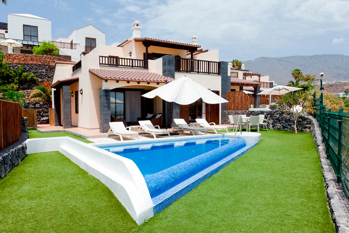 Villa with pool and sun loungers in Tenerife, surrounded by greenery and mountains.
