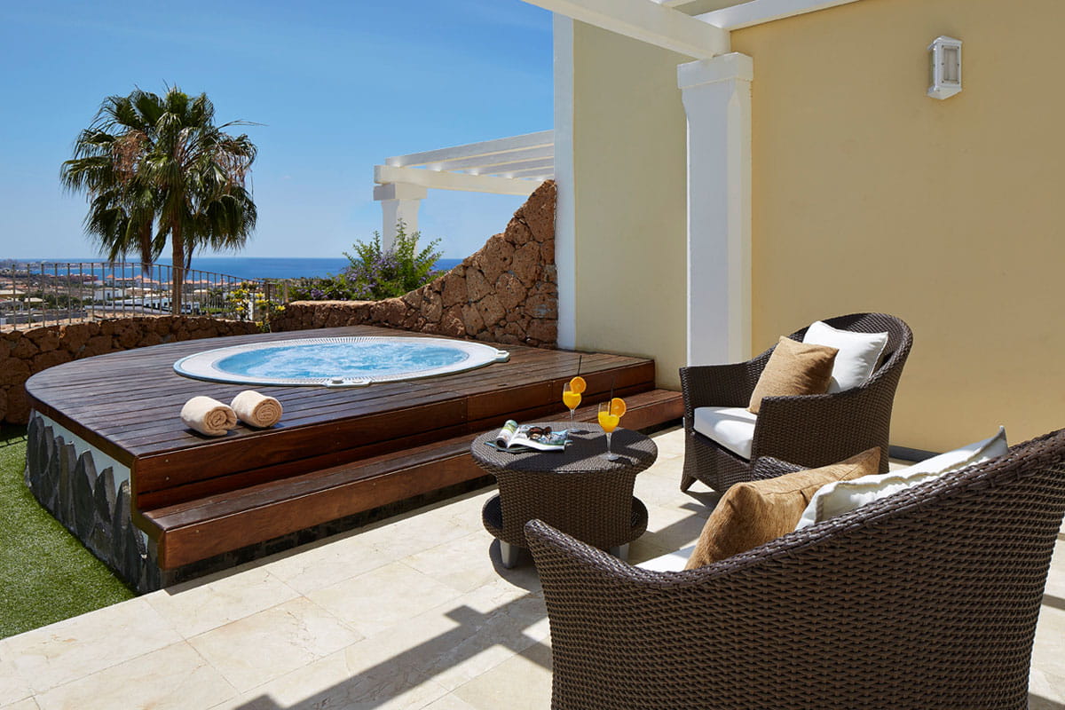 Jacuzzi on terrace with sea view in Tenerife, surrounded by wicker chairs and palm tree.