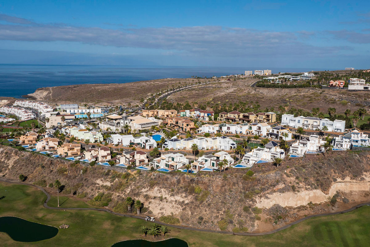 Aerial view of a residential area by the coast in Tenerife, with green fields and the ocean.