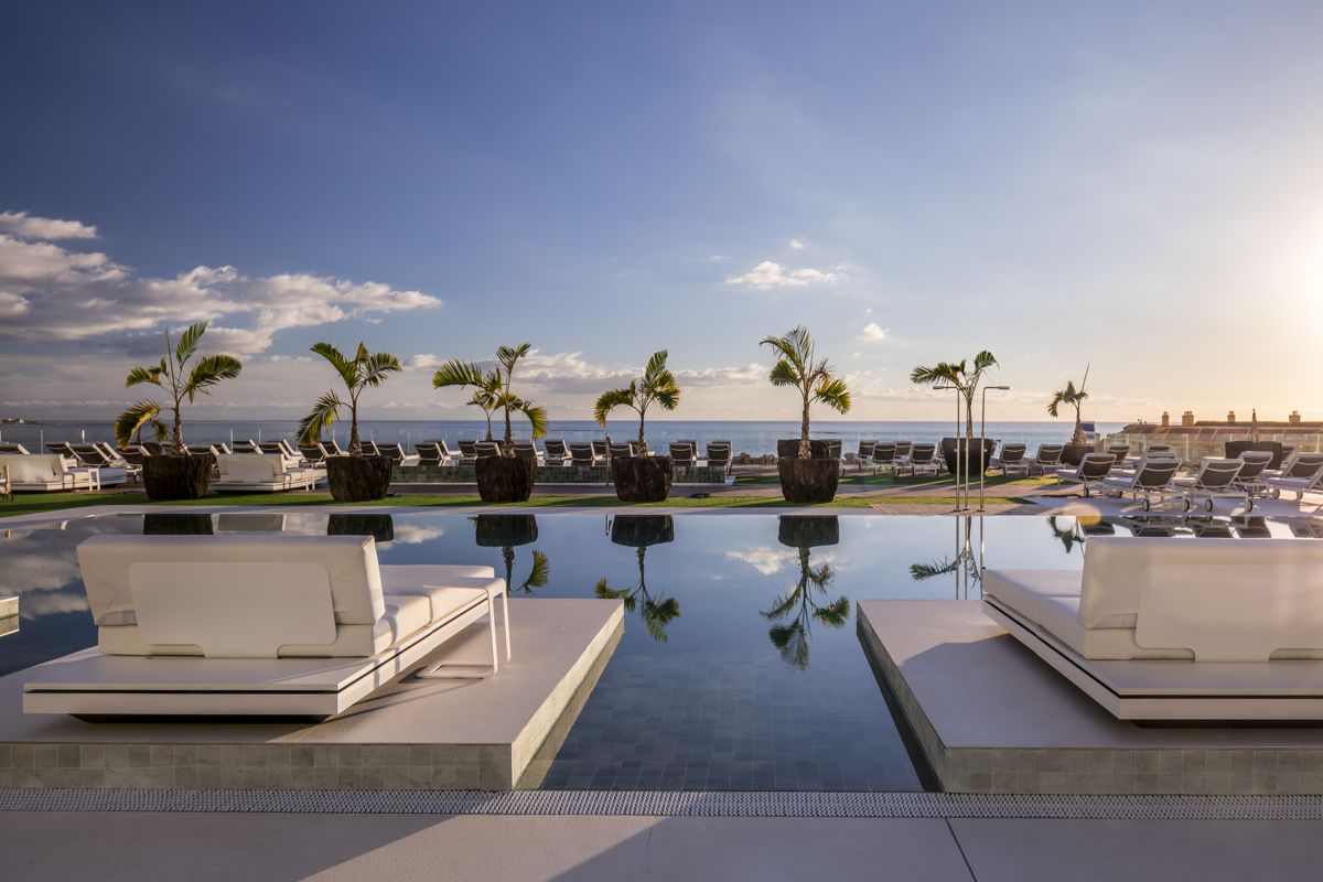 Poolside lounge chairs and palm trees overlooking ocean at sunset in Tenerife.
