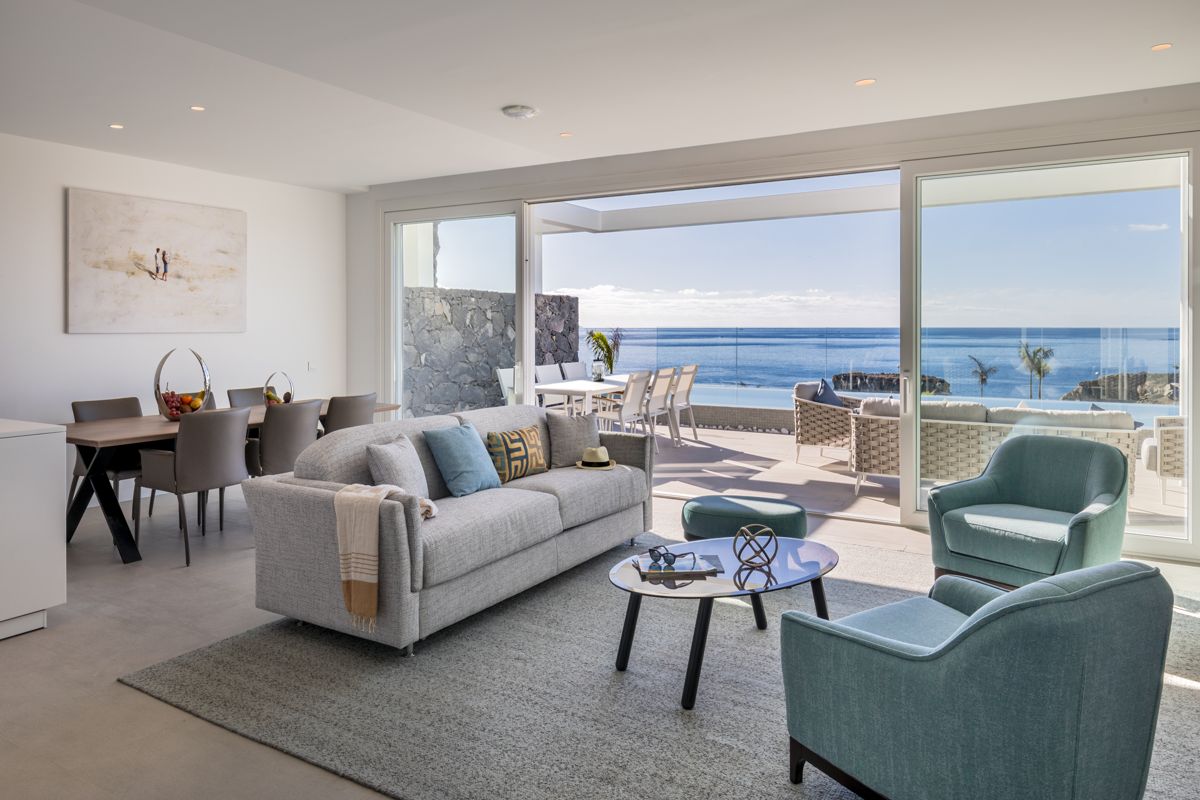 Contemporary living room overlooking ocean in Tenerife, featuring gray sofa and blue chairs.