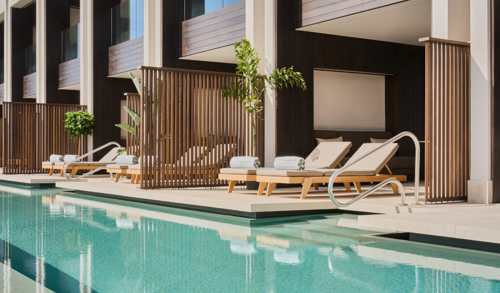 Sun loungers by a modern pool in Tenerife with wooden privacy panels.