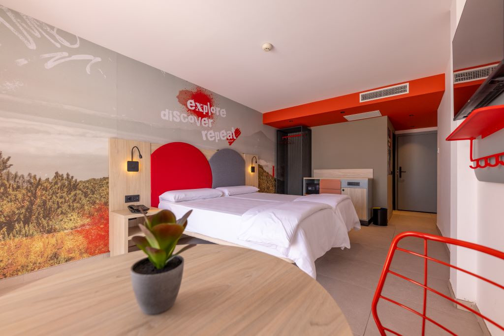 Modern room with double bed, floor plan and mural that says explore discover repeat.