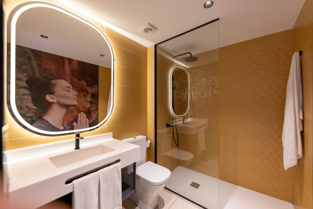 Bathroom with shower, sink, illuminated mirror and photograph of a woman meditating in Tenerife.