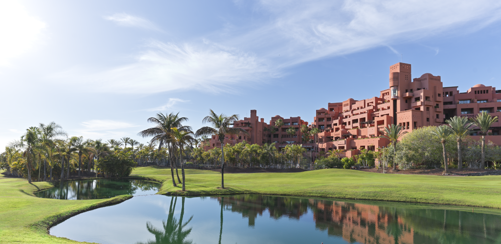 Red building with palm trees and pond in Tenerife under blue sky.