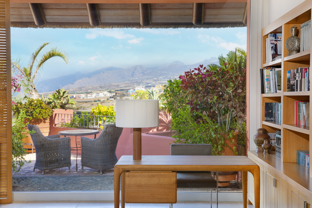 Sunny terrace view over Adeje mountains with palm trees and outdoor seating.