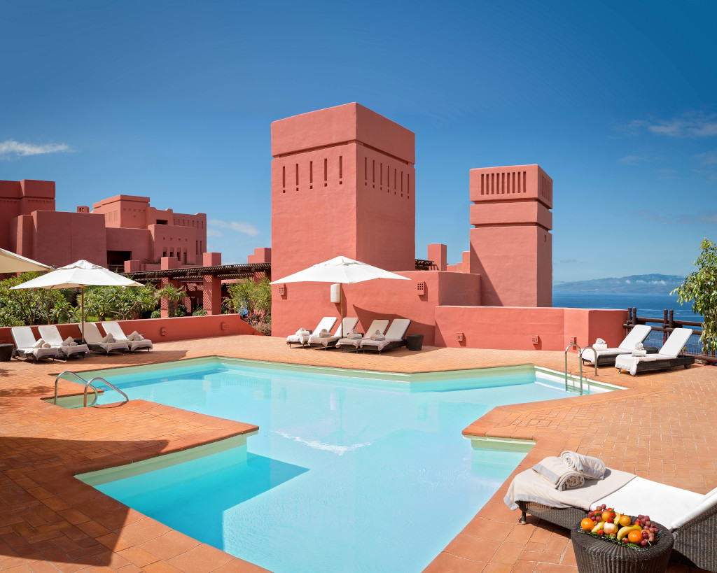 Outdoor pool with sun loungers and red buildings in Tenerife.