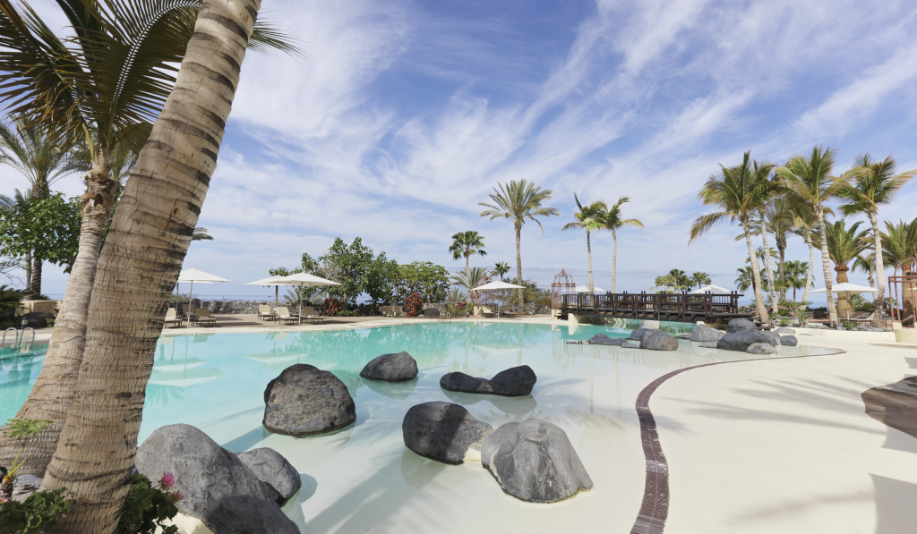 Outdoor swimming pool surrounded by palm trees and rocks in Tenerife.