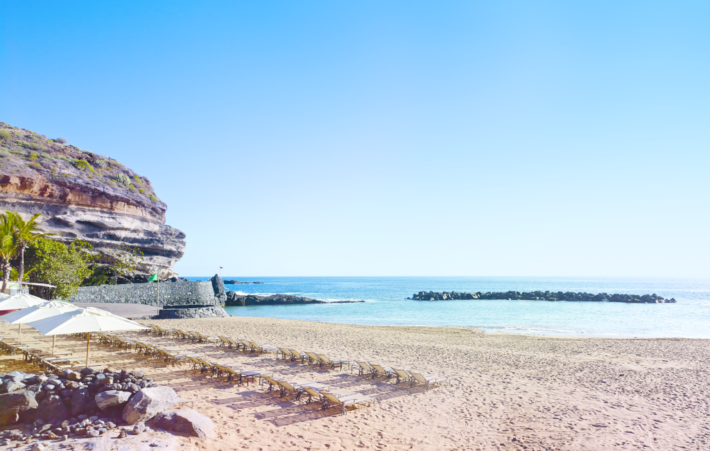 Sunloungers and umbrellas on the sandy beach at Tenerife with blue ocean.