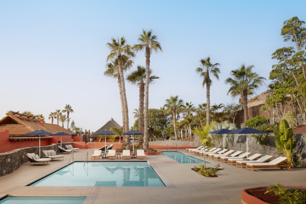 Outdoor pool area with loungers, umbrellas, and palm trees at a Tenerife resort.