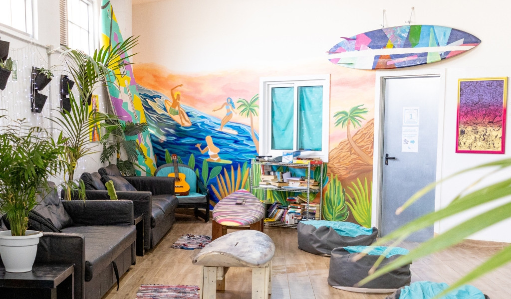 Colorful lounge with surf decor, wall mural, couches, plants, and bean bags in Tenerife.