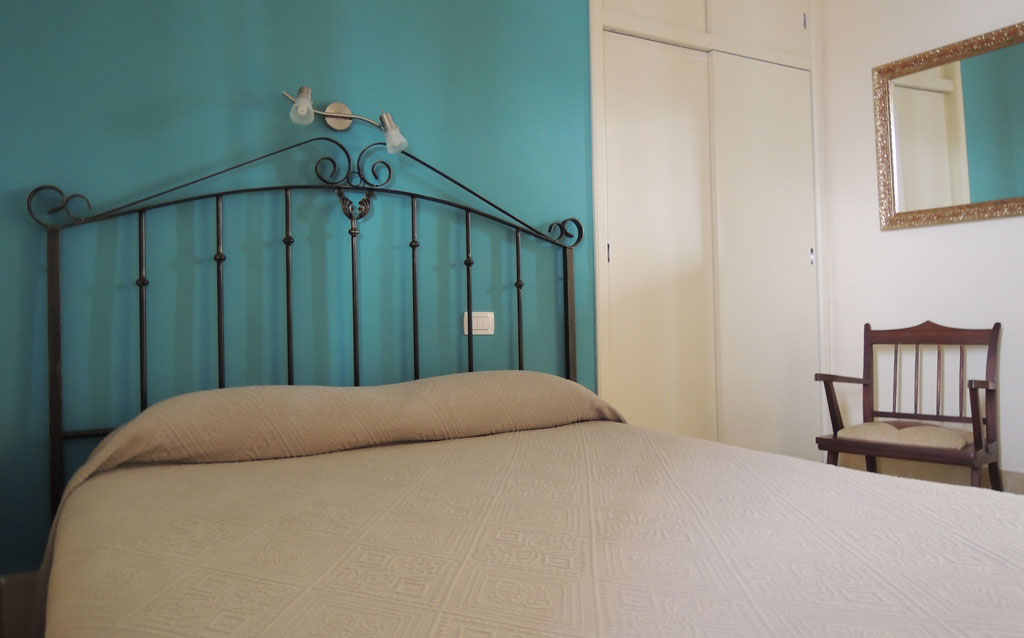 Bedroom with metal bed frame, teal wall, chair, and mirror in La Laguna, Tenerife.