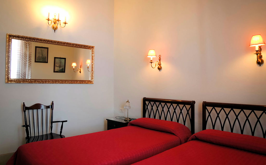 Twin beds with red covers, wall lamps, and a mirror in a room in Tenerife.
