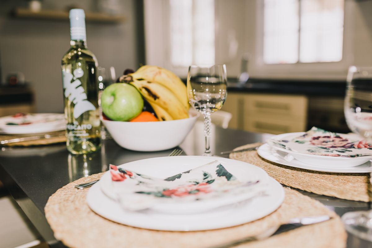Dining table with plates, floral napkins, a bowl of fruit, and a wine bottle in Tenerife kitchen.