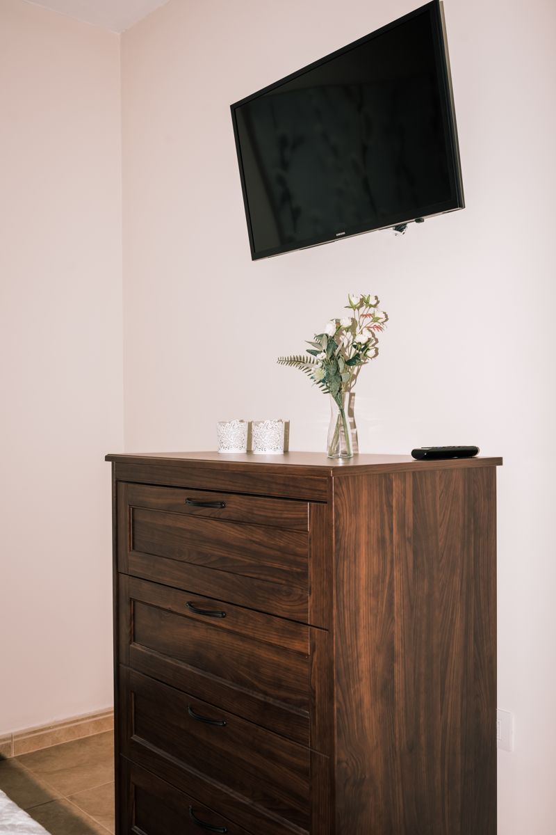 Wall-mounted TV over wooden dresser with vase and small dishes in a Tenerife room.