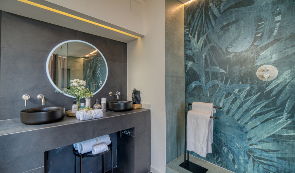 Modern bathroom with round mirror, double sinks, and tropical mural in Tenerife.