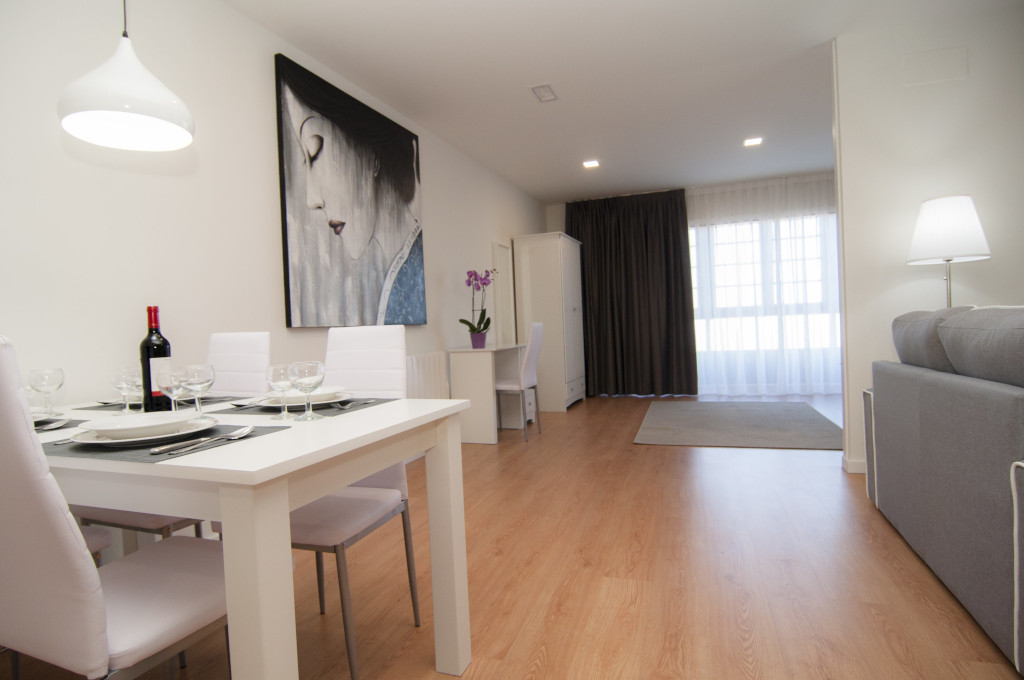 Dining room with table set, wine bottle, painting and sofa in Tenerife apartment.