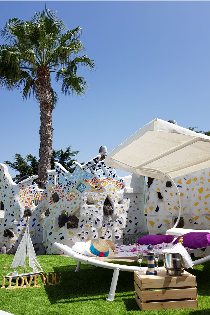 Palm tree, mosaic wall, and chaise lounge with straw hat in Tenerife garden.
