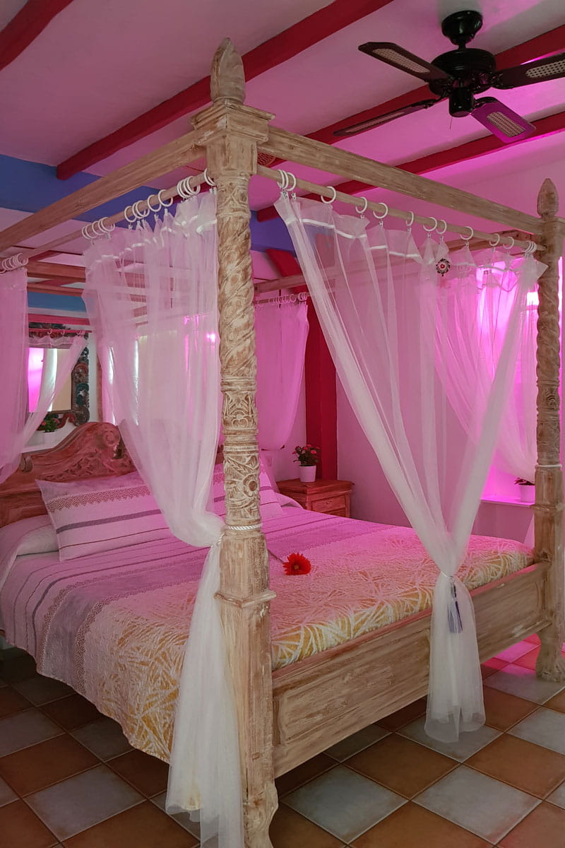 Four-poster bed with drapes and pink lighting in a cozy Tenerife room.