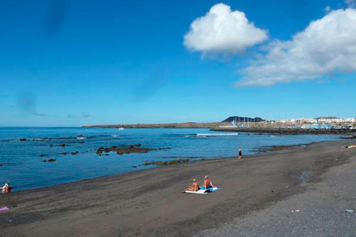 Sandy beach with people sunbathing, ocean and town in the background, Tenerife.