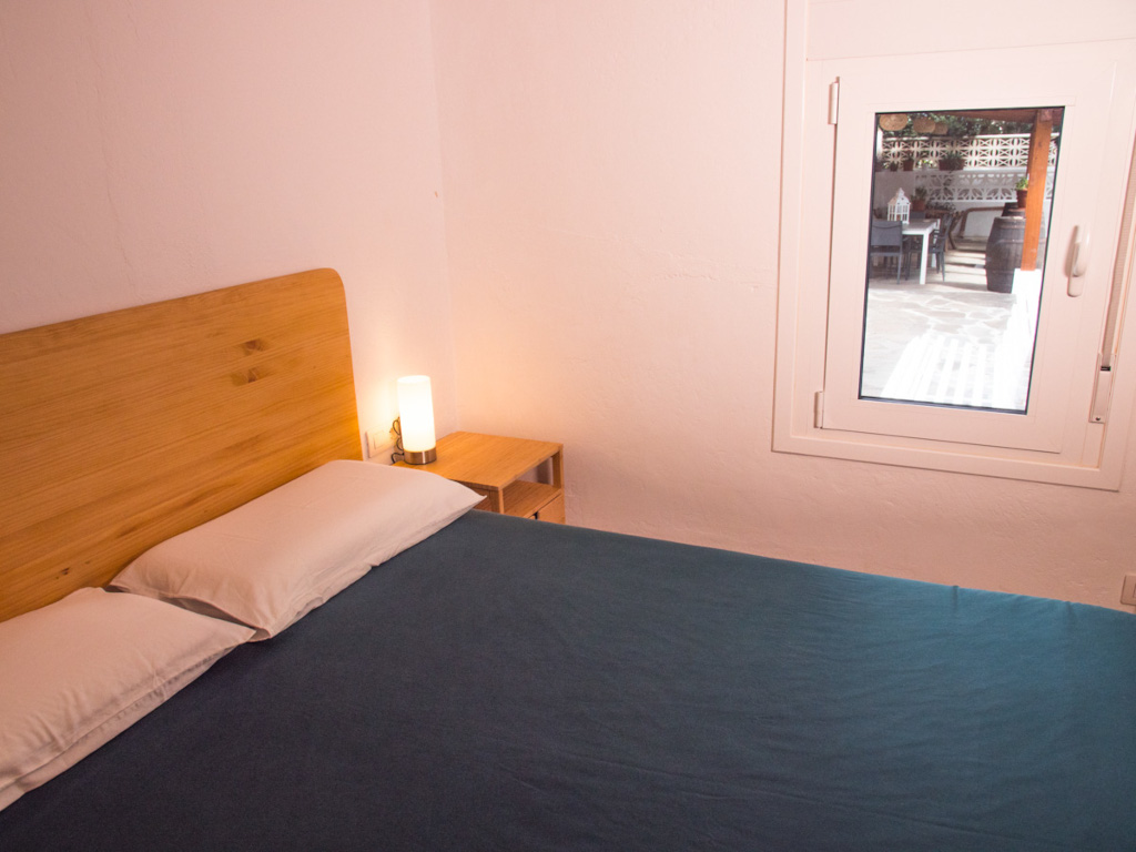 Bed with blue sheets and wooden headboard near window in Tenerife room.