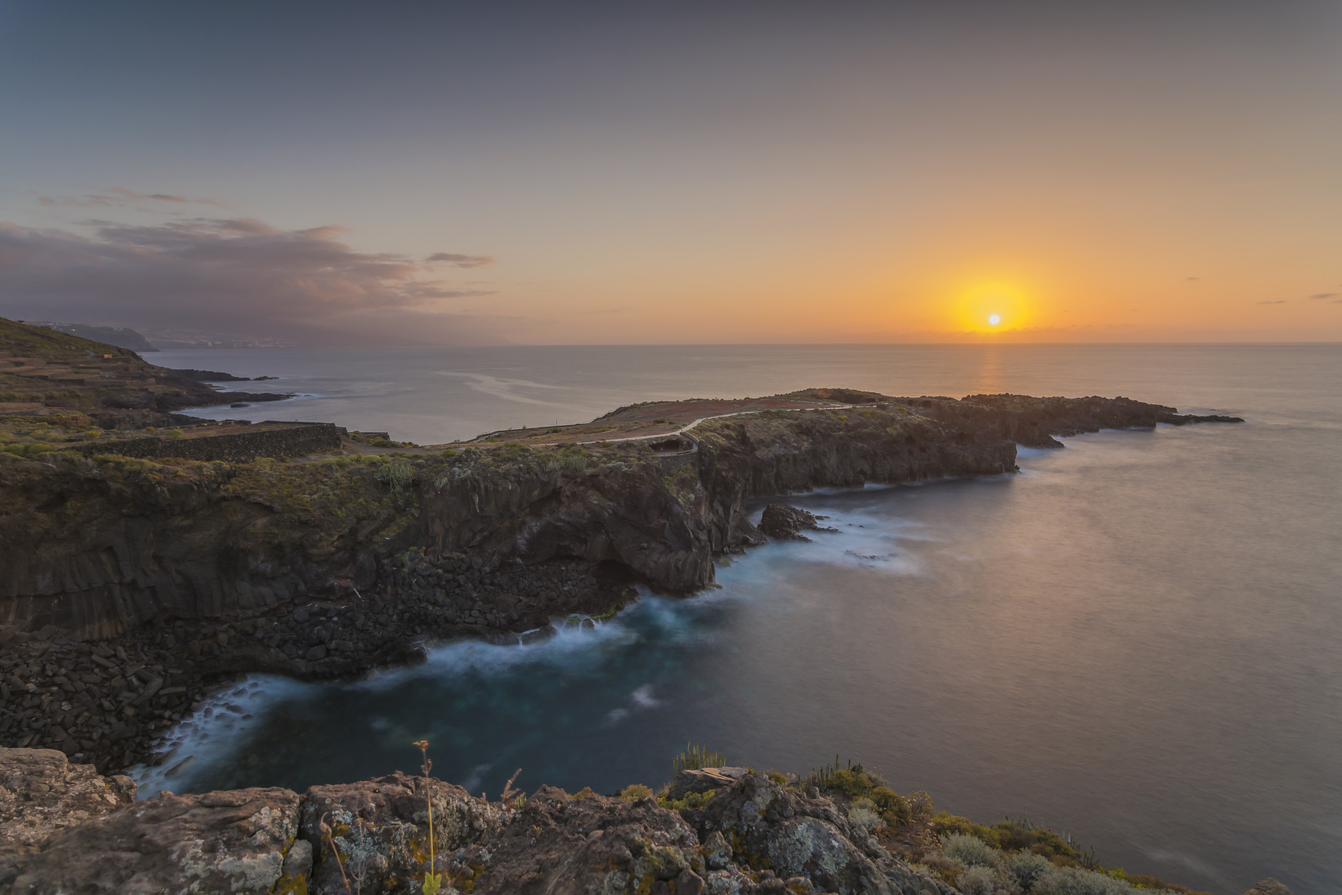 Sunset on the coast of Tenerife with cliffs and sea on the horizon.
