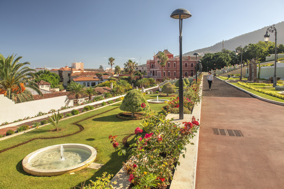 Gardens and red building in Puerto de la Cruz, Tenerife, with mountains in the background.
