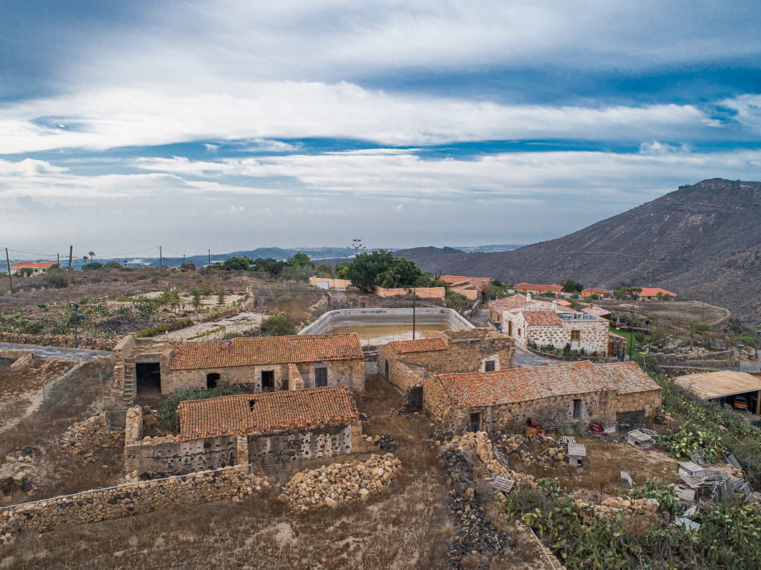 Ruins of old rock houses with tiled roofs in Tenerife, surrounded by countryside.