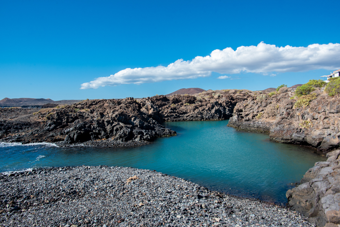 Natural pool of turquoise water in Los Abrigos, surrounded by volcanic rocks.