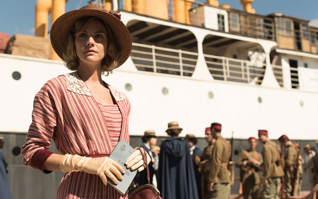 Woman wearing hat and gloves in front of a boat, people around in Tenerife.