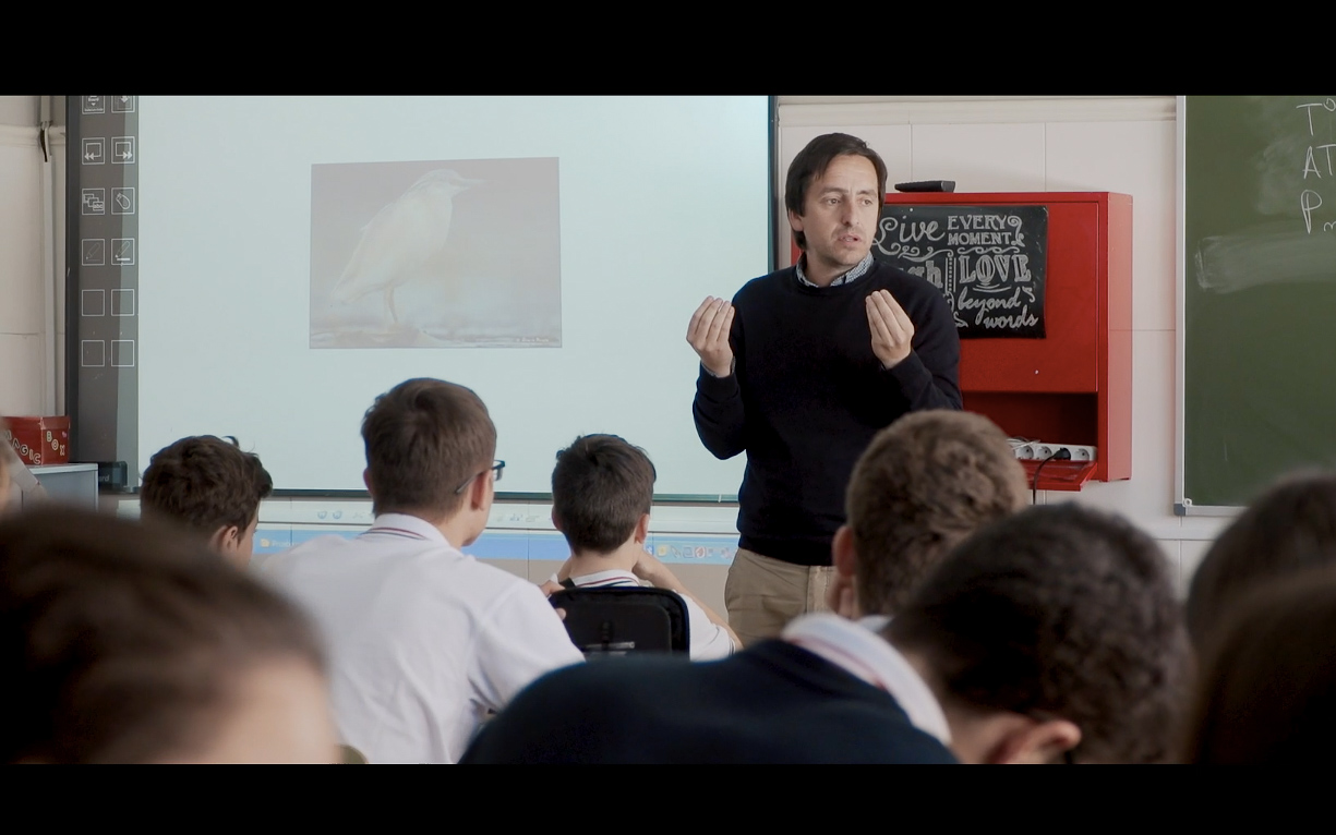 Teacher lecturing in front of students with bird image on screen.