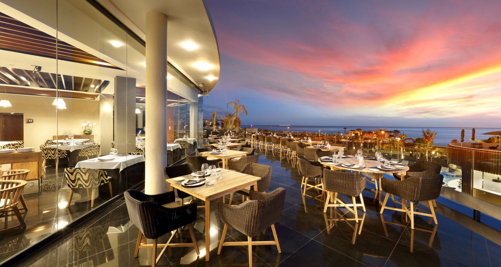 Restaurant with terrace at sunset in Tenerife, with sea view and prepared tables.